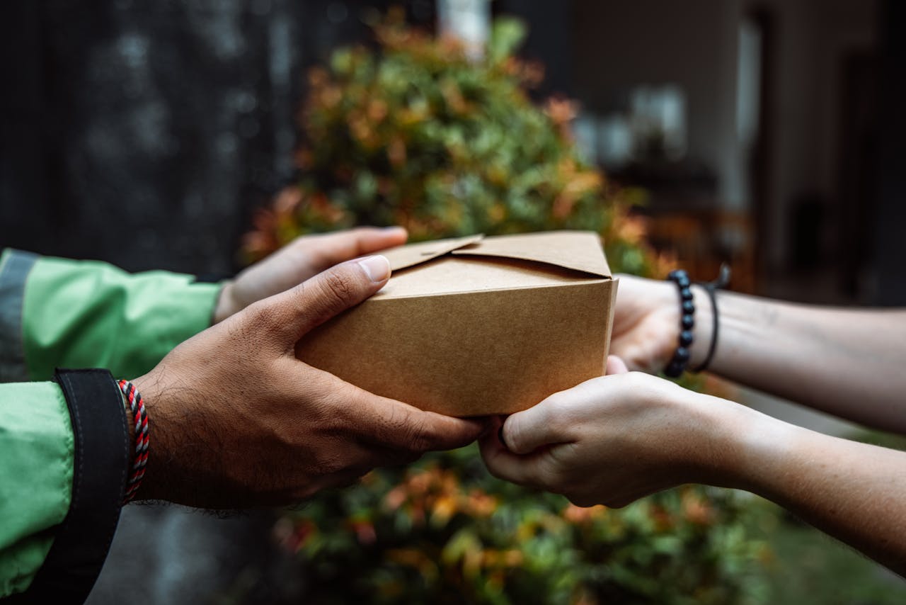 Close-up of hands exchanging a cardboard box, symbolizing delivery service outdoors.